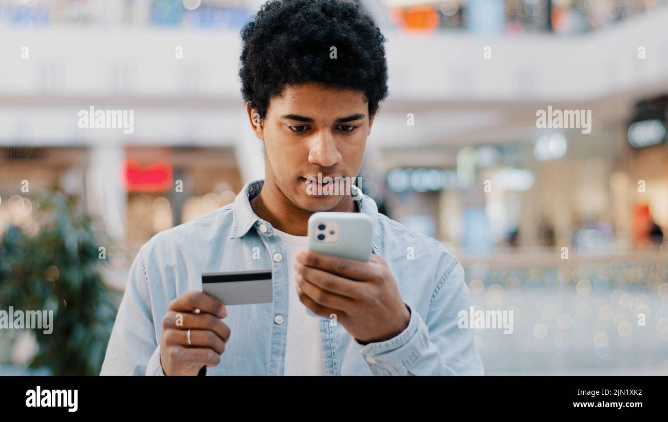 Il tipo domenicano africano che fa la transazione di shopping in linea nell'uomo di rete con il telefono inserisce i problemi di numero di carta con l'errore finanziario nell'app mobile Foto Stock