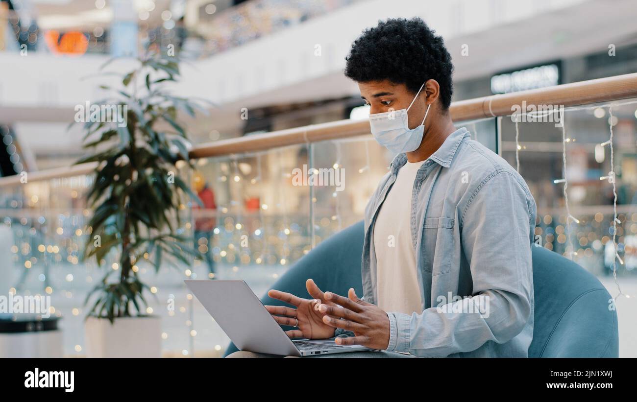 African american uomo in faccia medico maschera ufficio azienda luogo di lavoro videochiamata con portatile covid epidemia online insegnante tutor consulente remoto Foto Stock