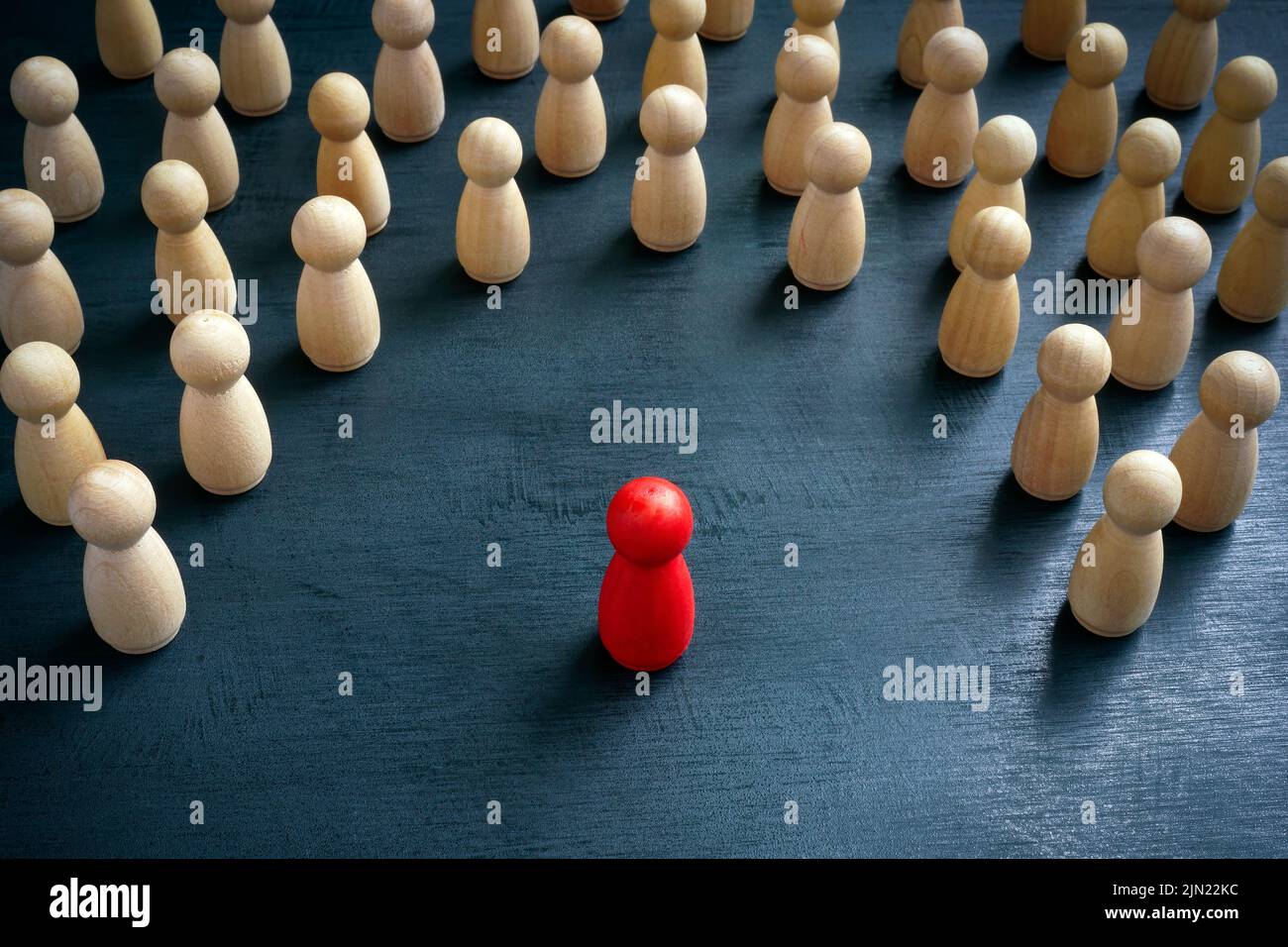 Concetto di discriminazione e inclusione. Le figurine in legno circondavano quella rossa. Foto Stock