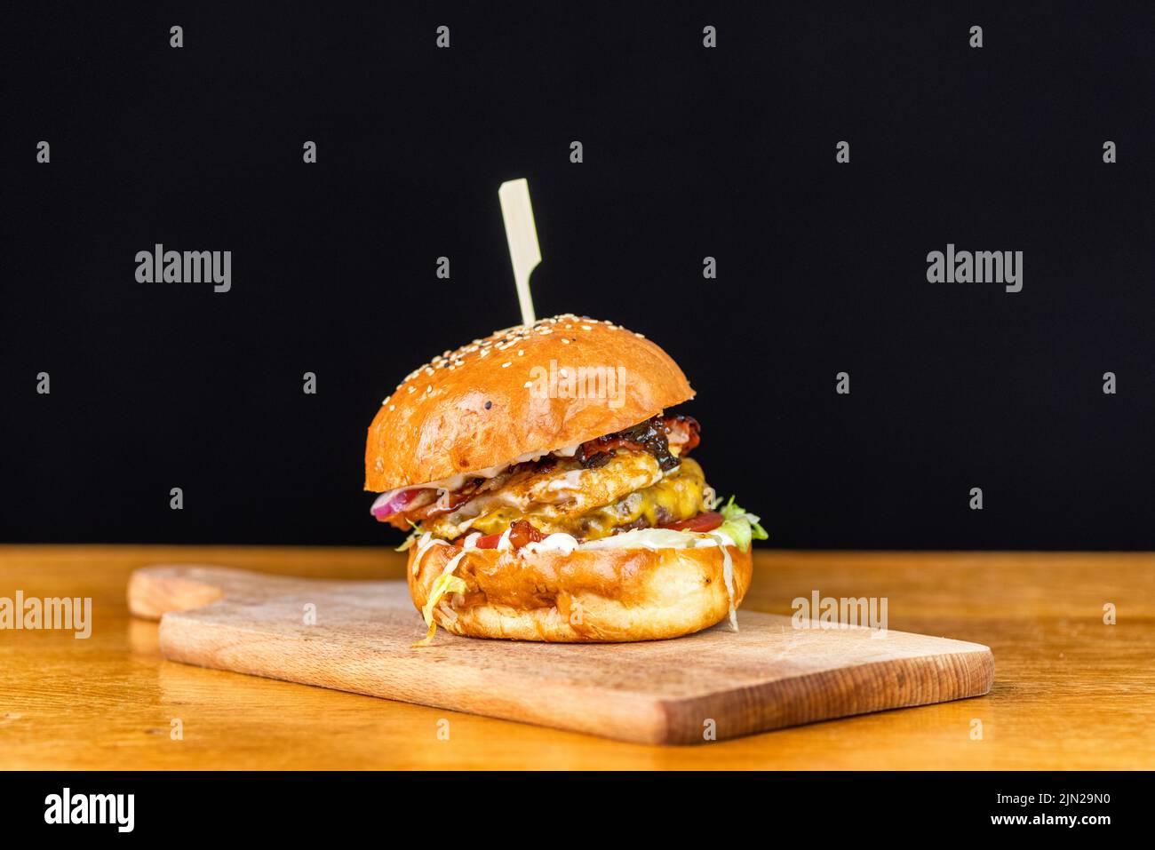 Close-up di freschi e deliziosi fatti in casa burger con lattuga, formaggio, cipolla e pomodoro su un rustico di asse di legno su uno sfondo scuro Foto Stock
