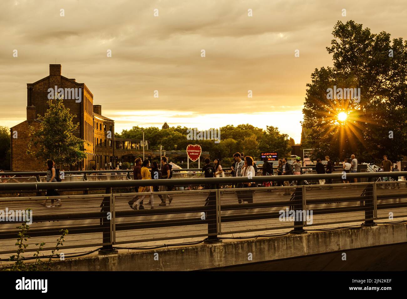 Un gruppo di persone casuali che passano davanti al Kings Cross Plaza Bridge durante il tramonto. Foto Stock