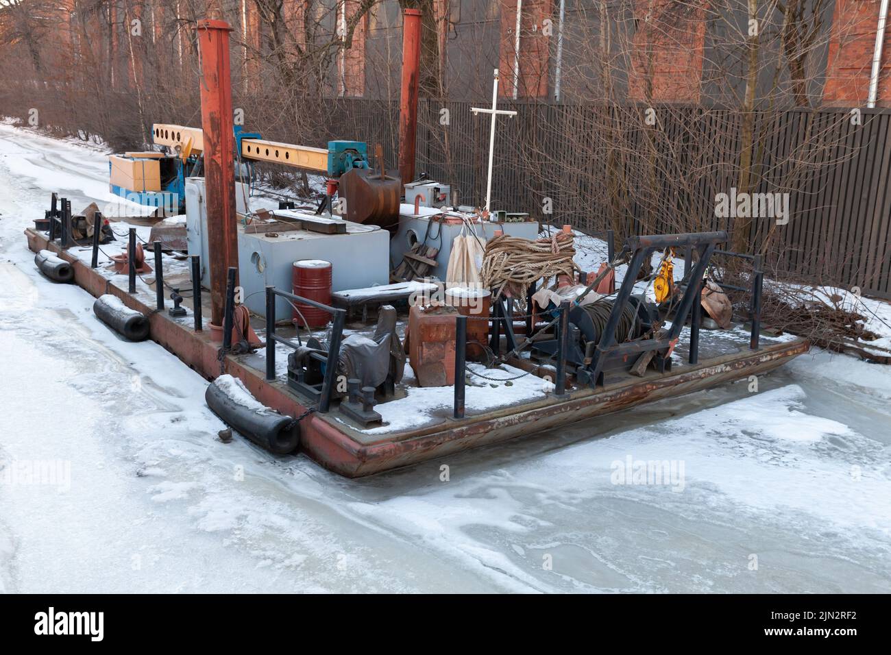 Piccola gru galleggiante e barca di servizio è ormeggiata su un fiume ghiacciato a San Pietroburgo, Russia Foto Stock