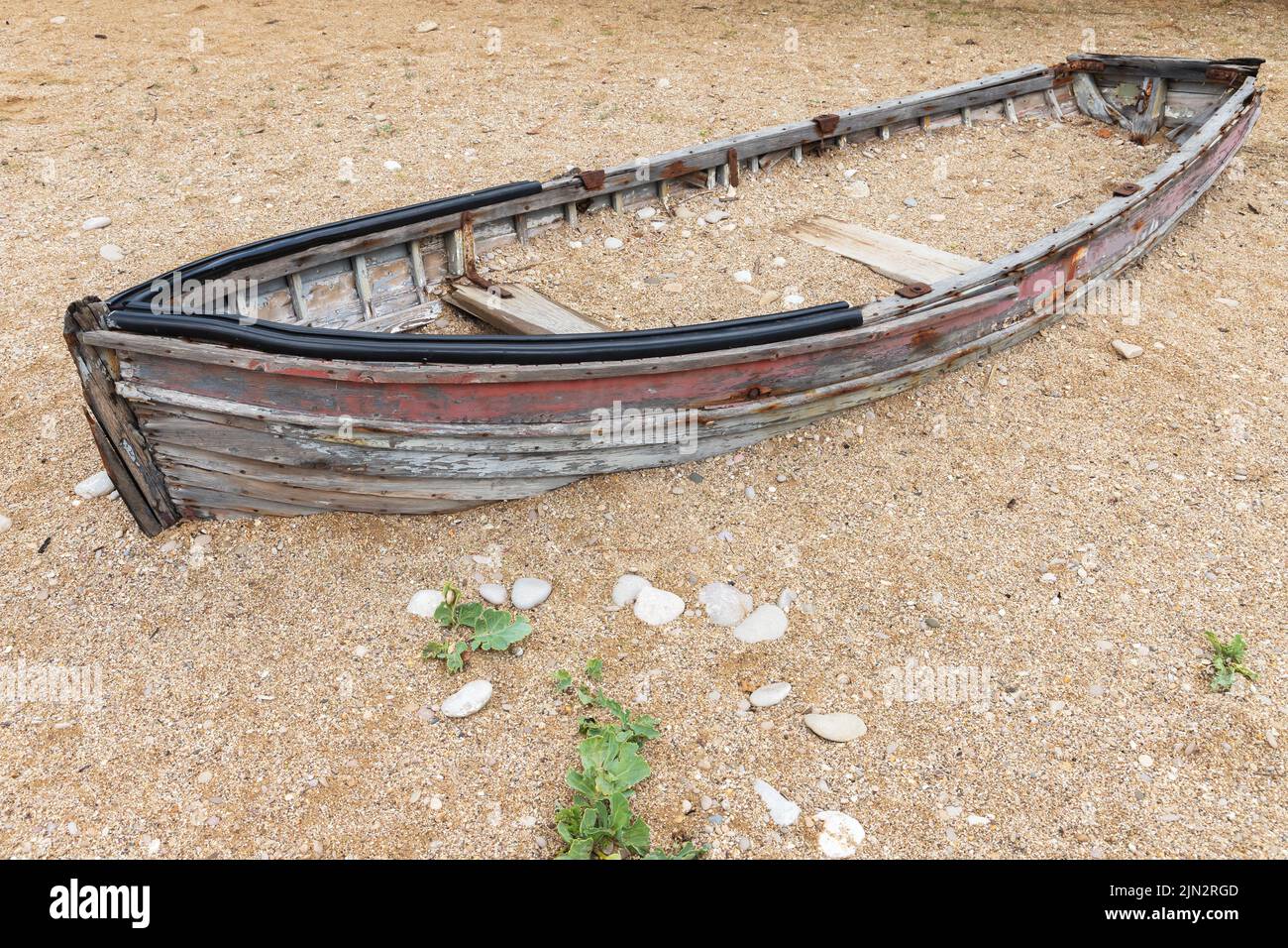 Una vecchia barca di legno abbandonata si trova su una costa sabbiosa vuota durante il giorno Foto Stock