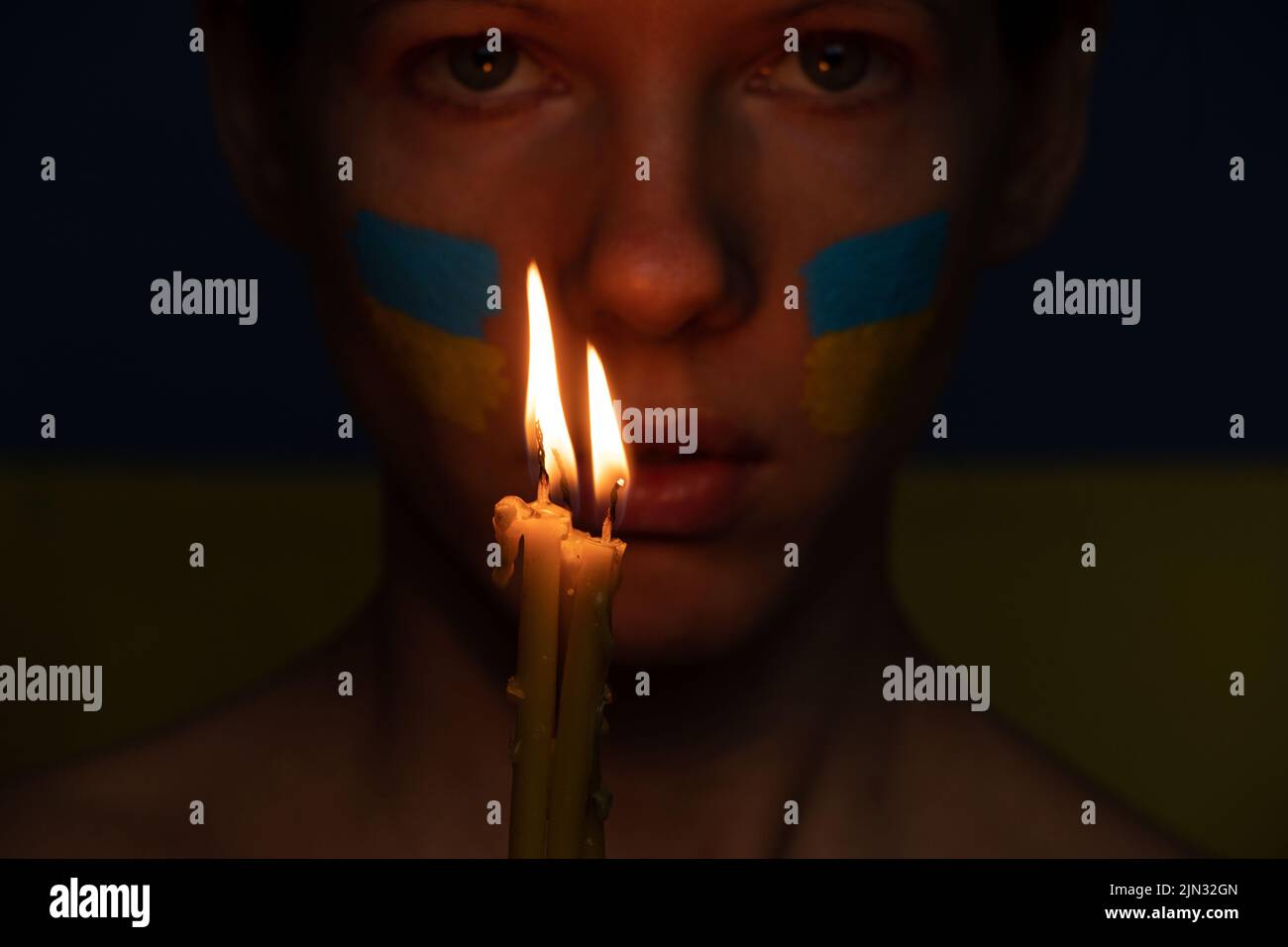 Il volto della ragazza con la bandiera nazionale dell'Ucraina giallo-blu sul volto dello sfondo della fiamma della candela, patriota, pace in Ucraina, preghiera per Foto Stock