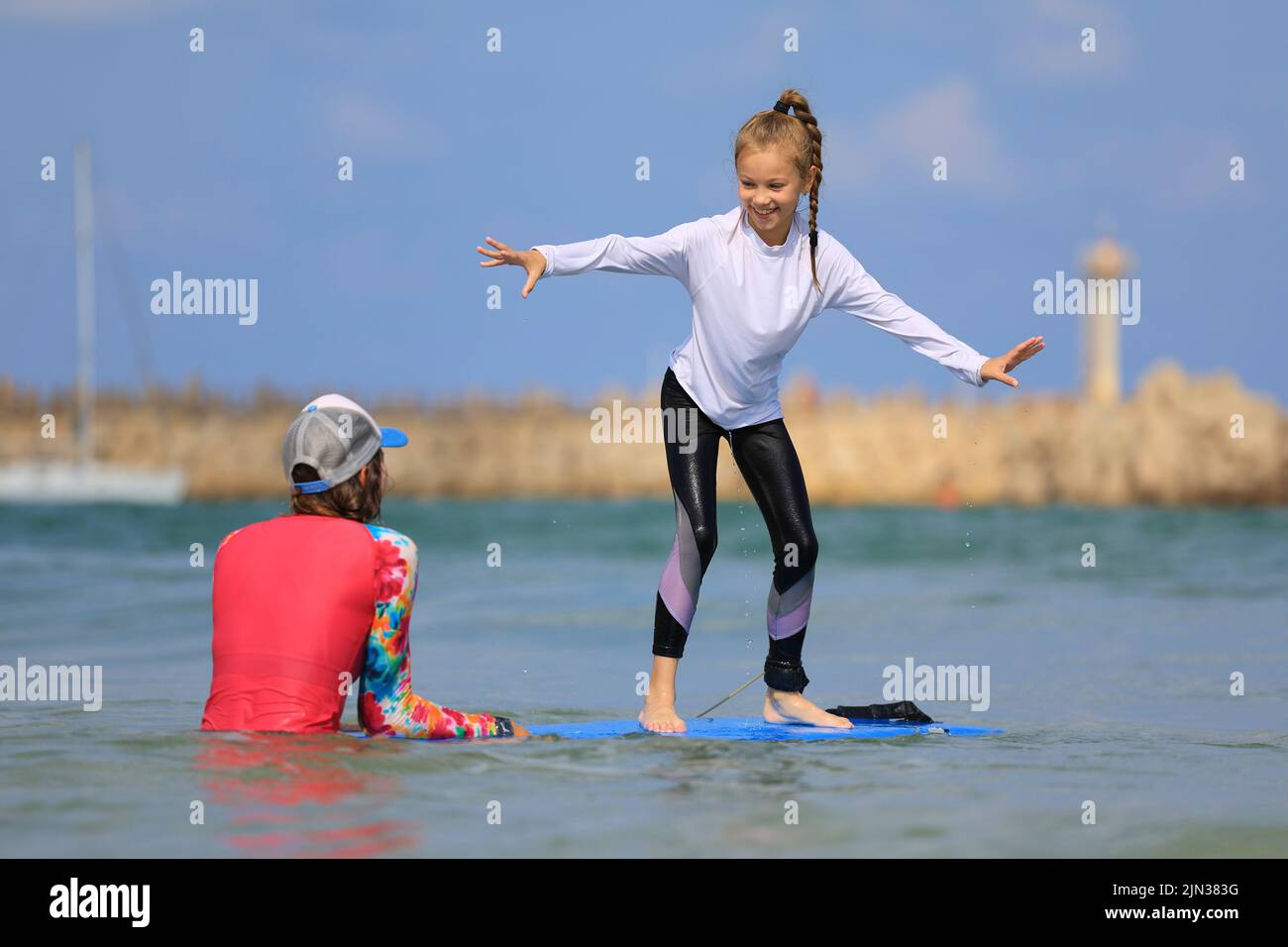 i giovani surfisti imparano a cavalcare su una tavola da surf con un istruttore alla scuola di surf. Stile di vita familiare attivo, lezioni di sport acquatici per bambini Foto Stock