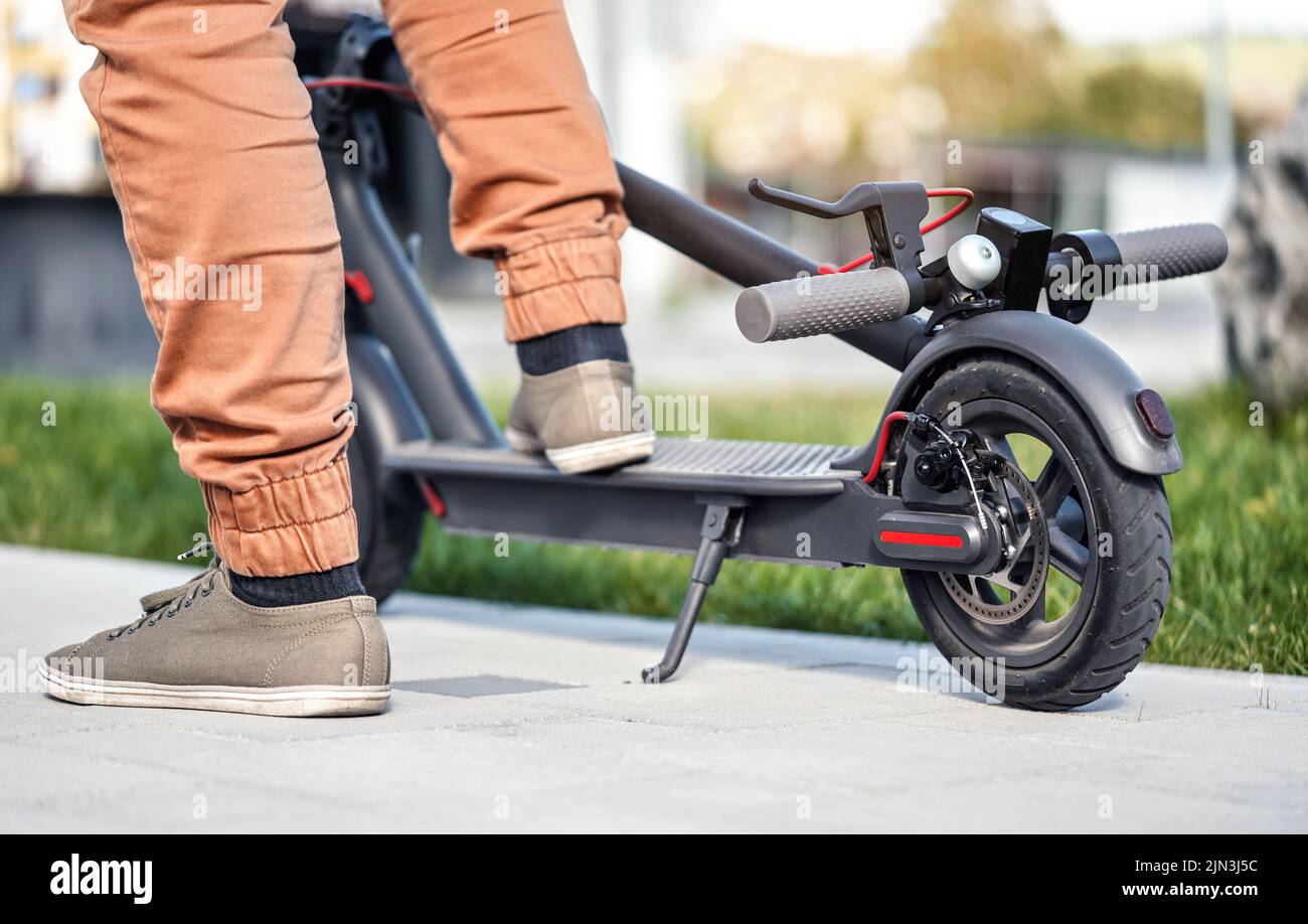 Uomo piedi su scooter elettrico parcheggiato, primo piano dettaglio, luce del sole erba sfocata sullo sfondo Foto Stock