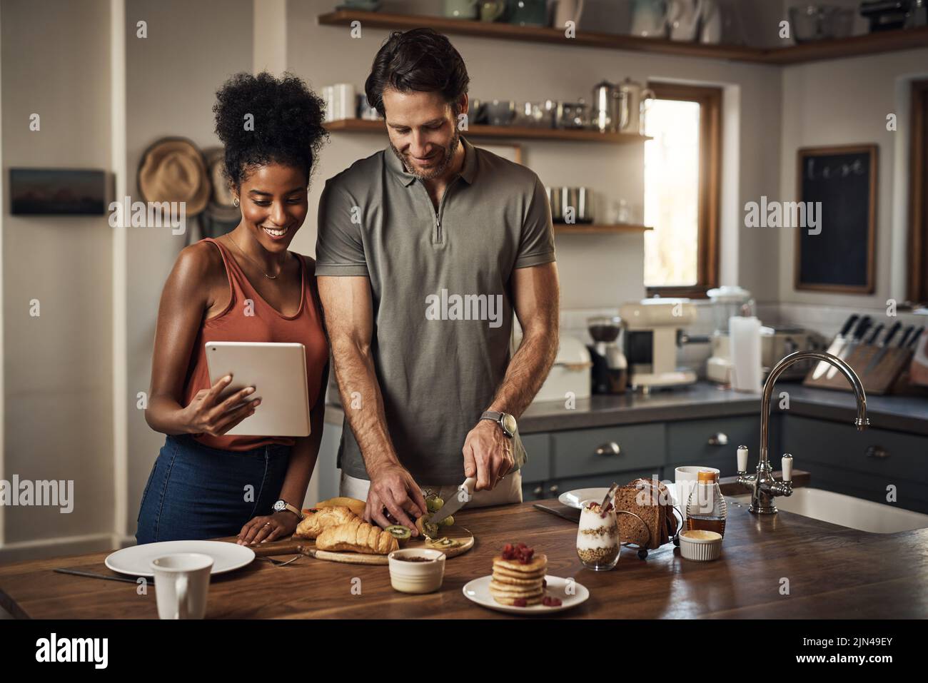 La colazione di cucina della coppia con un tablet mentre cerca le ricette ed i video in linea sul Internet. Felici gli amanti interrazziali che preparano un sano Foto Stock