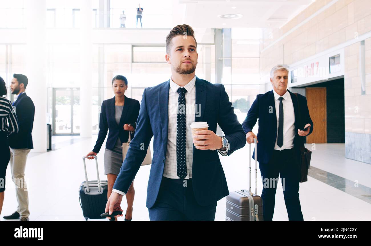Porta con te la prossima grande avventura lavorativa: Tre uomini d'affari camminano e tirano le valigie mentre sono in ufficio durante il giorno. Foto Stock