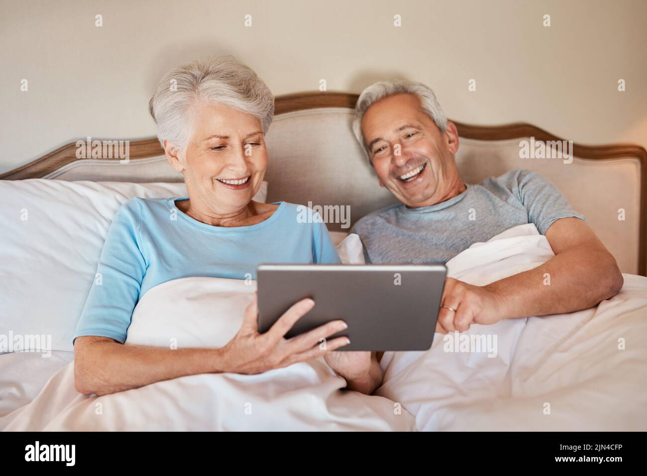 Che cosa ne pensate. Una coppia anziana felice seduta insieme a letto e usando un tablet in una casa di cura. Foto Stock