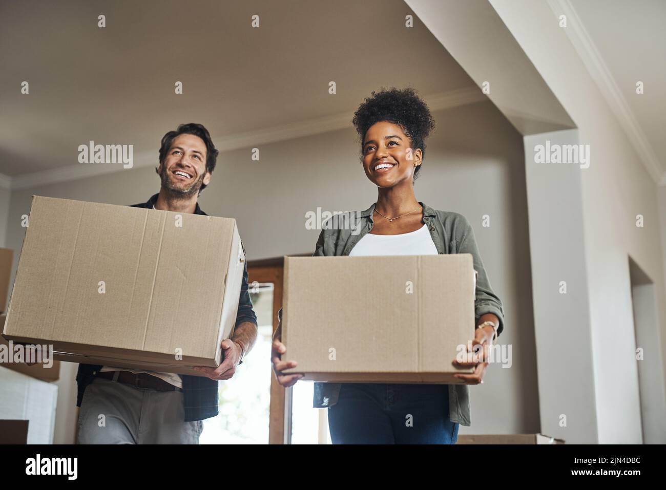 Sono davvero entusiasta di iniziare a decorare. Una giovane coppia sorride mentre porta le scatole nella loro nuova casa. Foto Stock