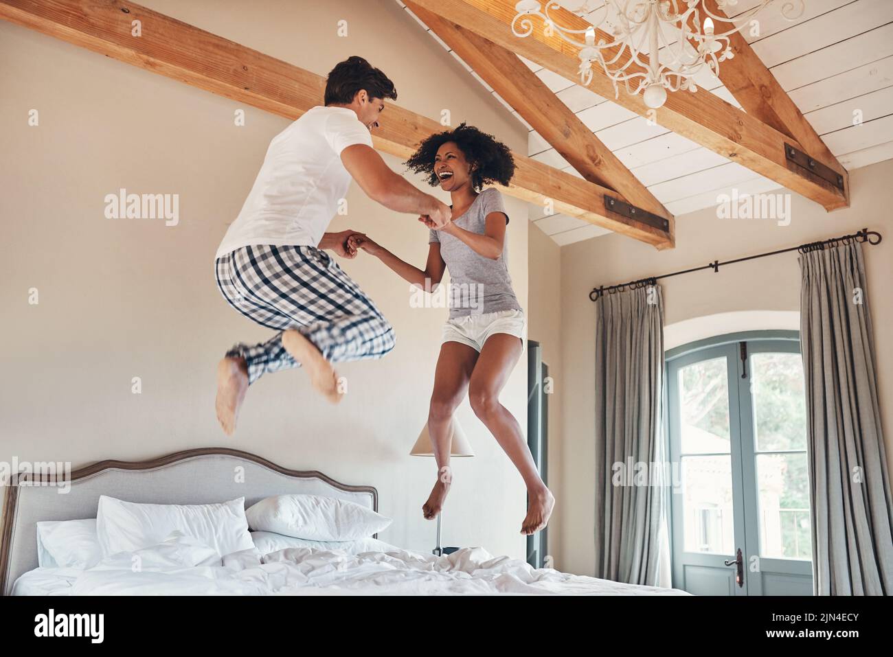 Stavano facendo un salto di fede insieme. Sho a tutta lunghezza di una giovane coppia giocosa che salta sul letto insieme a casa. Foto Stock