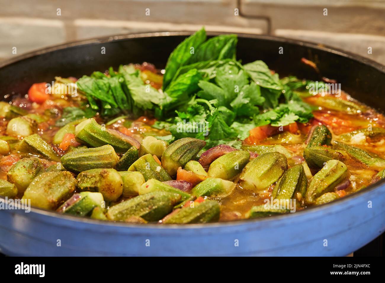 Le cipolle di okra e viola fritte sono fritte in padella con coriandolo e basilico su stufa a gas Foto Stock
