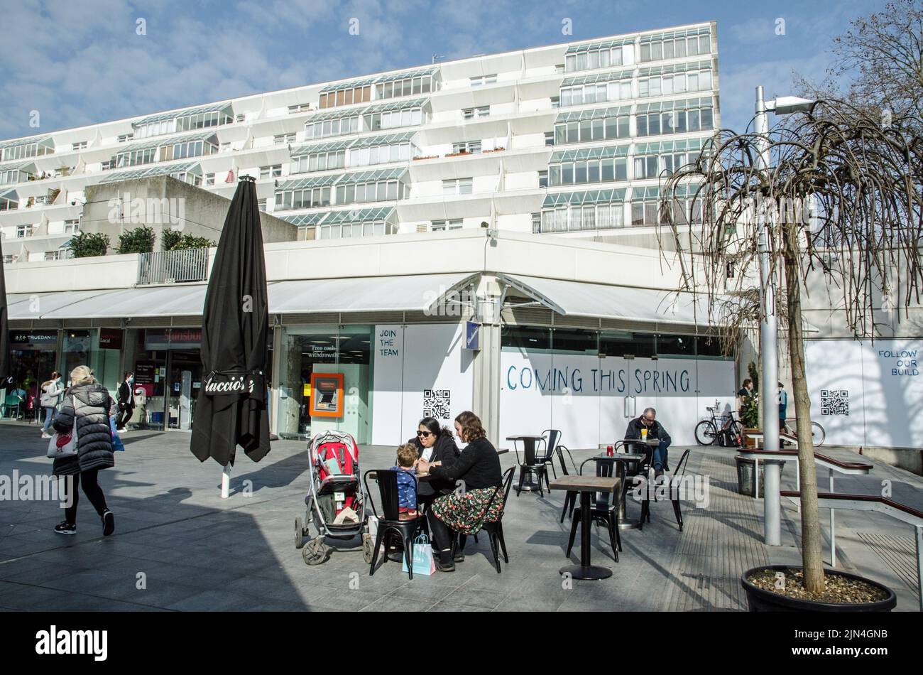 Londra, Regno Unito - 21 marzo 2022: Gli amanti dello shopping si godono il sole ai tavoli da caffè allestiti nel Brunswick Centre di Bloomsbury, nel centro di Londra. Il brutale Foto Stock