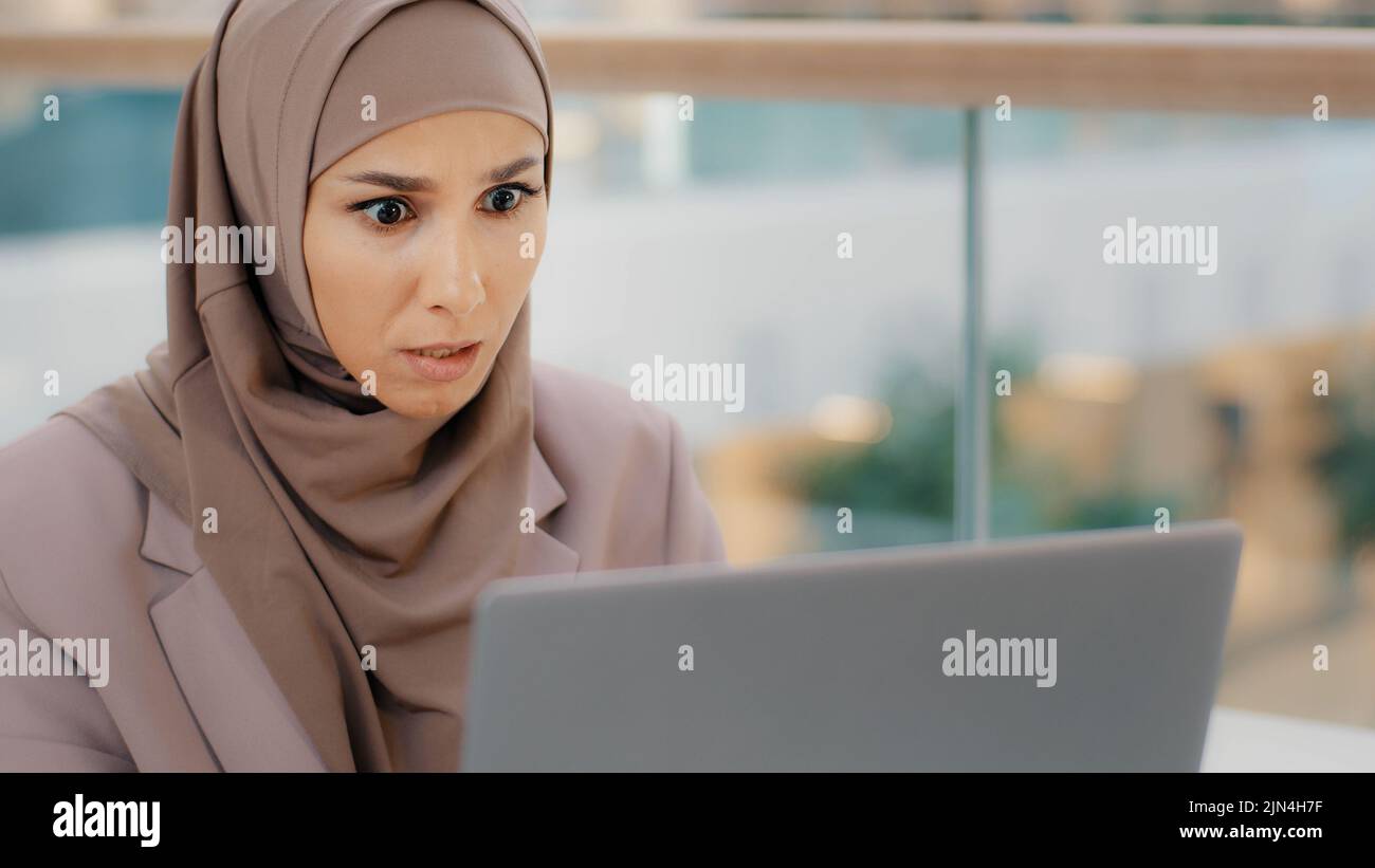 Giovane preoccupato ha sottolineato la donna d'affari araba in hijab guardando lo schermo del laptop sensazione di scioccato infastidito a causa del problema software guasto perdita di dati Foto Stock