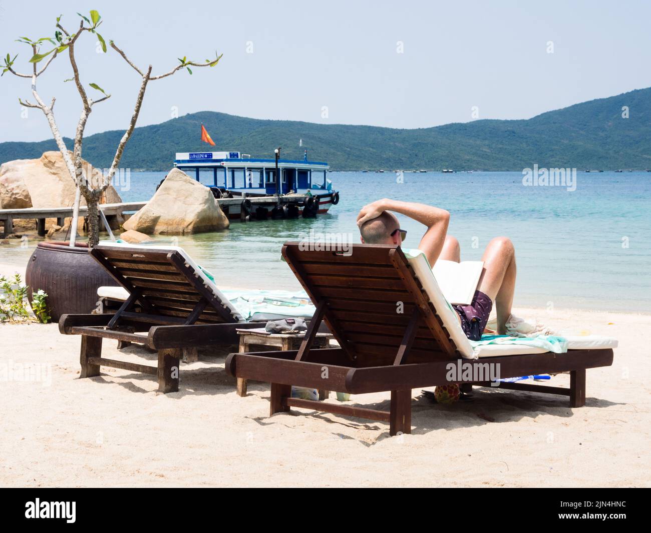 Van Ninh, Vietnam - 16 marzo 2016: Vacationer leggere un libro su una spiaggia di sabbia a Whale Island resort su una remota e isolata Whale Island Foto Stock