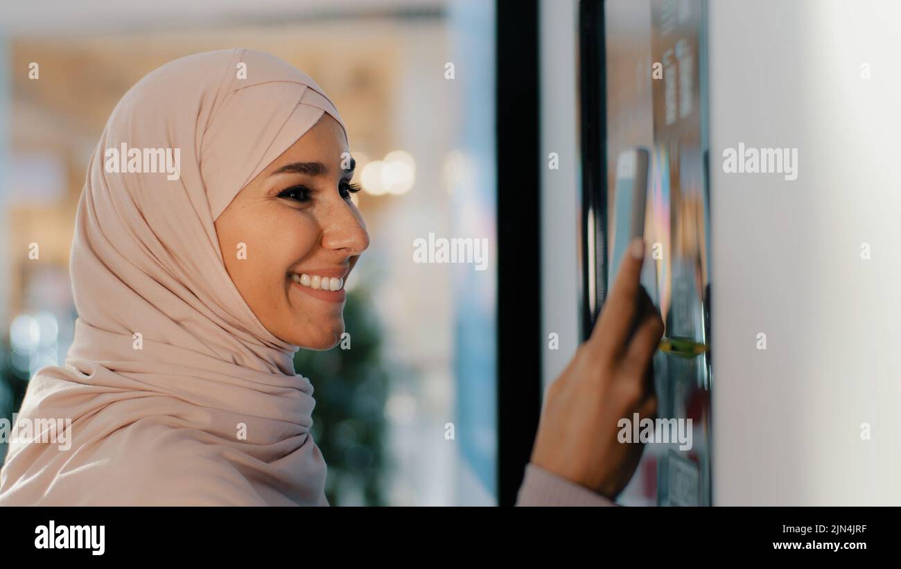 Giovane donna araba felice in hijab si trova vicino alla macchina da caffè ordini bere sorridente ragazza musulmana facendo ordine su automaton self-service paga per il servizio Foto Stock