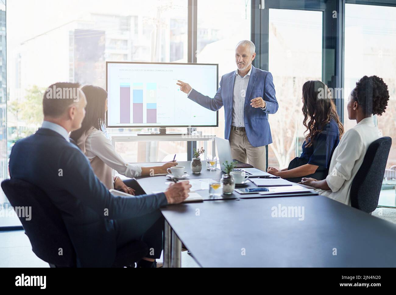 Il responsabile delle vendite presenta una presentazione sulla strategia di marketing e del marchio in una riunione della sala riunioni. Leader maschile maturo, aziendale e di successo punta a un Foto Stock