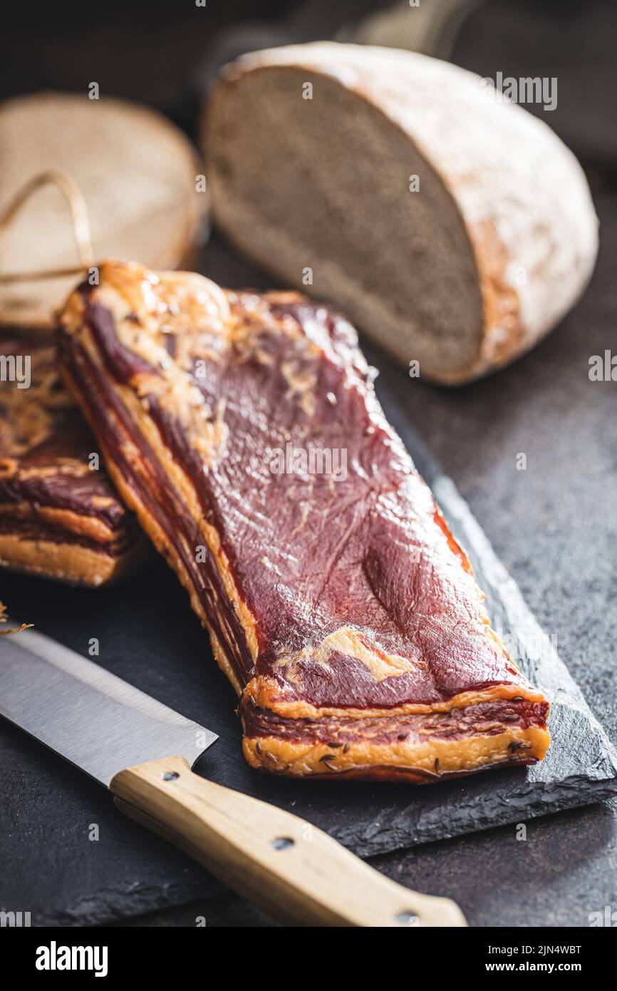 Pancetta affumicata intera su un tagliere. Foto Stock