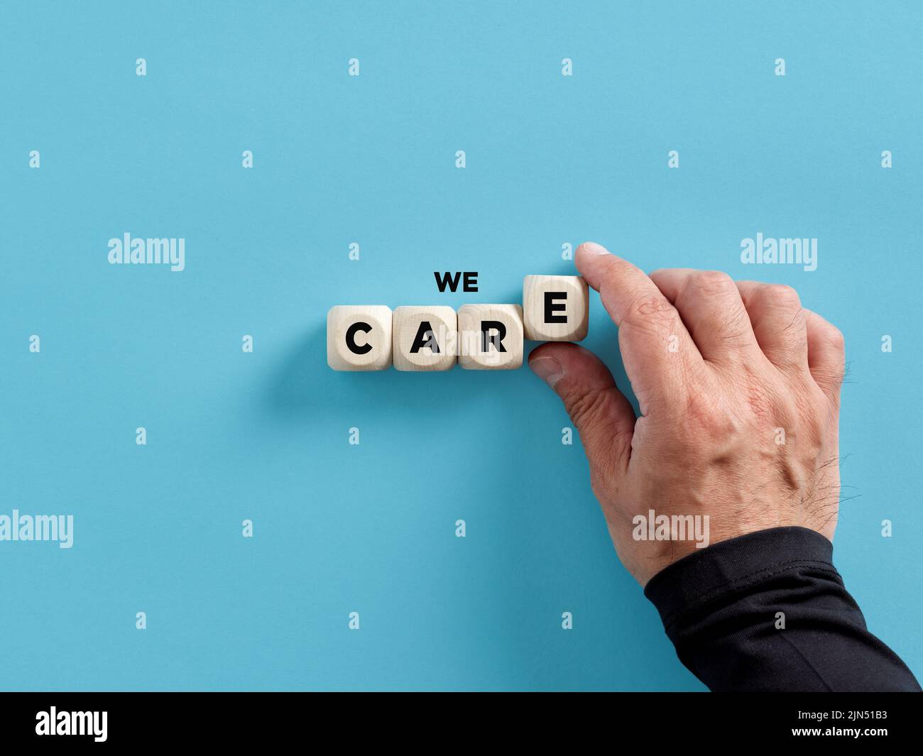 Maschio mano che arrangiano i cubi di legno con la parola che ci interessa. Dare cura, sostegno, assistenza, aiuto e fornire il concetto di bisogni. Foto Stock