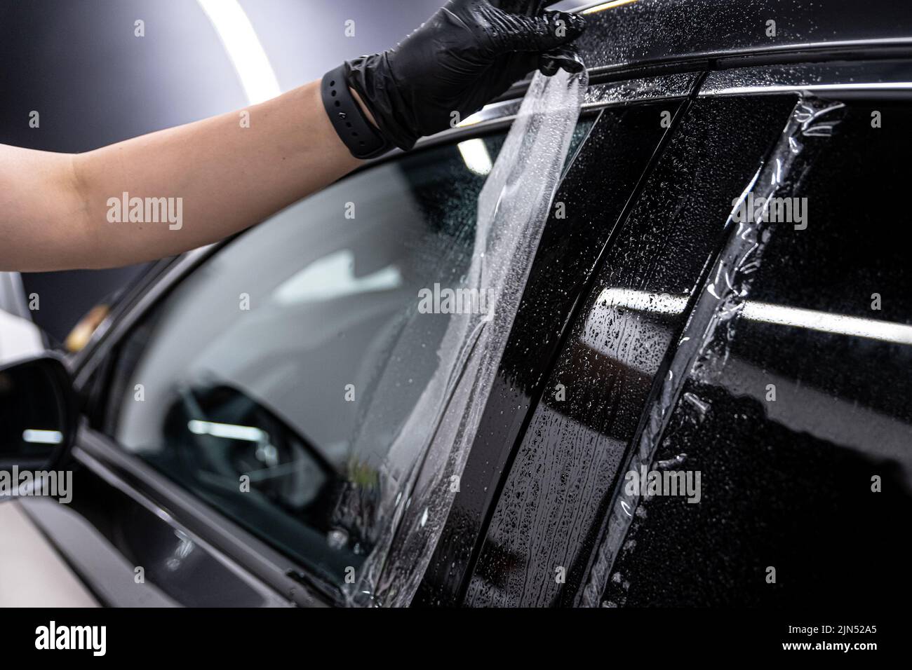 il dipendente dello studio dei dettagli dell'auto protegge la carrozzeria dell'auto con una pellicola protettiva Foto Stock