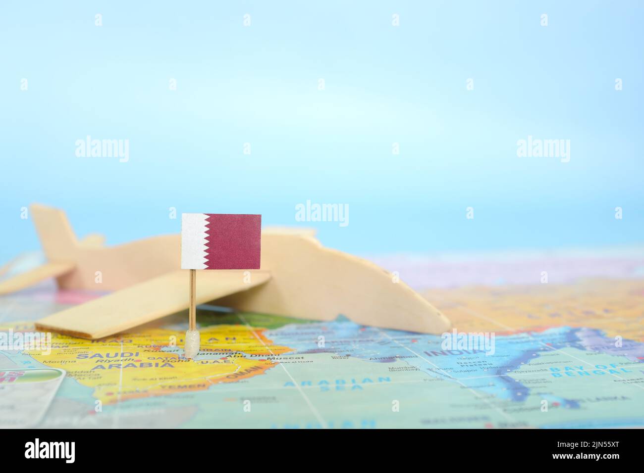 Fuoco selettivo della bandiera del Qatar in mappa del mondo sfocata e modello di aeroplano in legno. Qatar come concetto di viaggio e destinazione turistica. Foto Stock