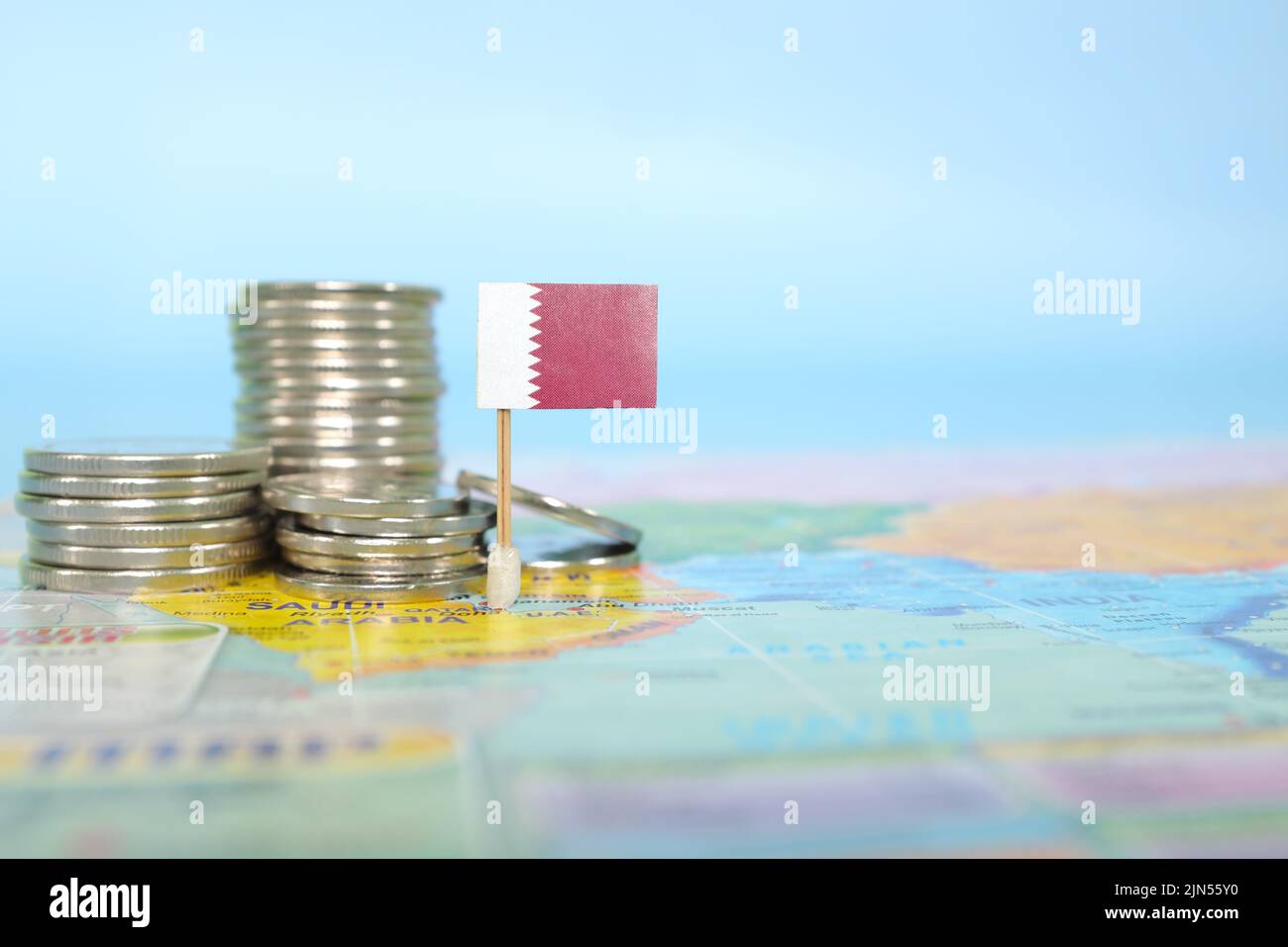 Fuoco selettivo della bandiera del Qatar nella mappa del mondo sfocata con le monete. Qatar economia e ricchezza concetto. Foto Stock