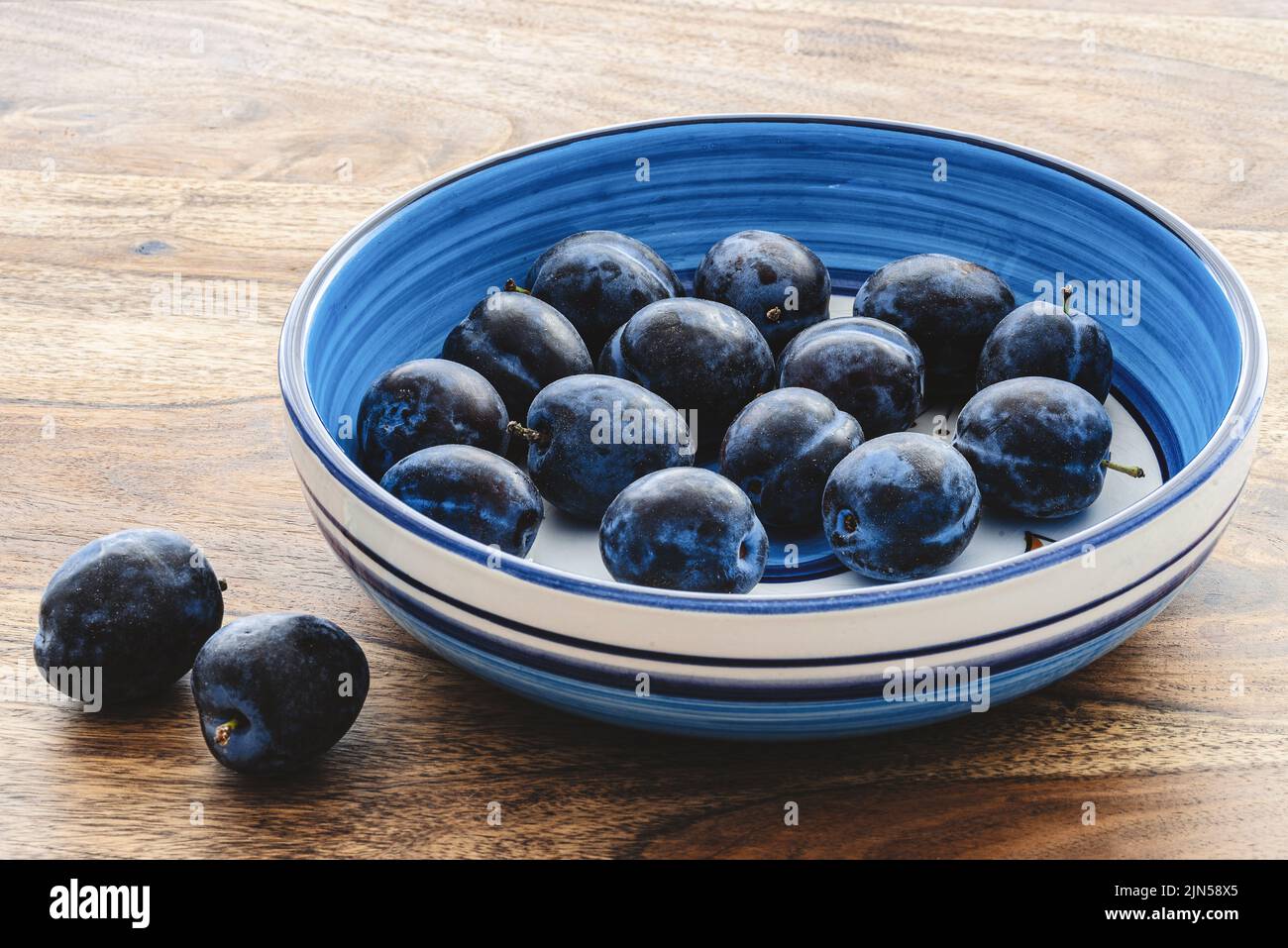 ciotola di ceramica blu riempita con prune fresche mature su tavola rustica di legno Foto Stock