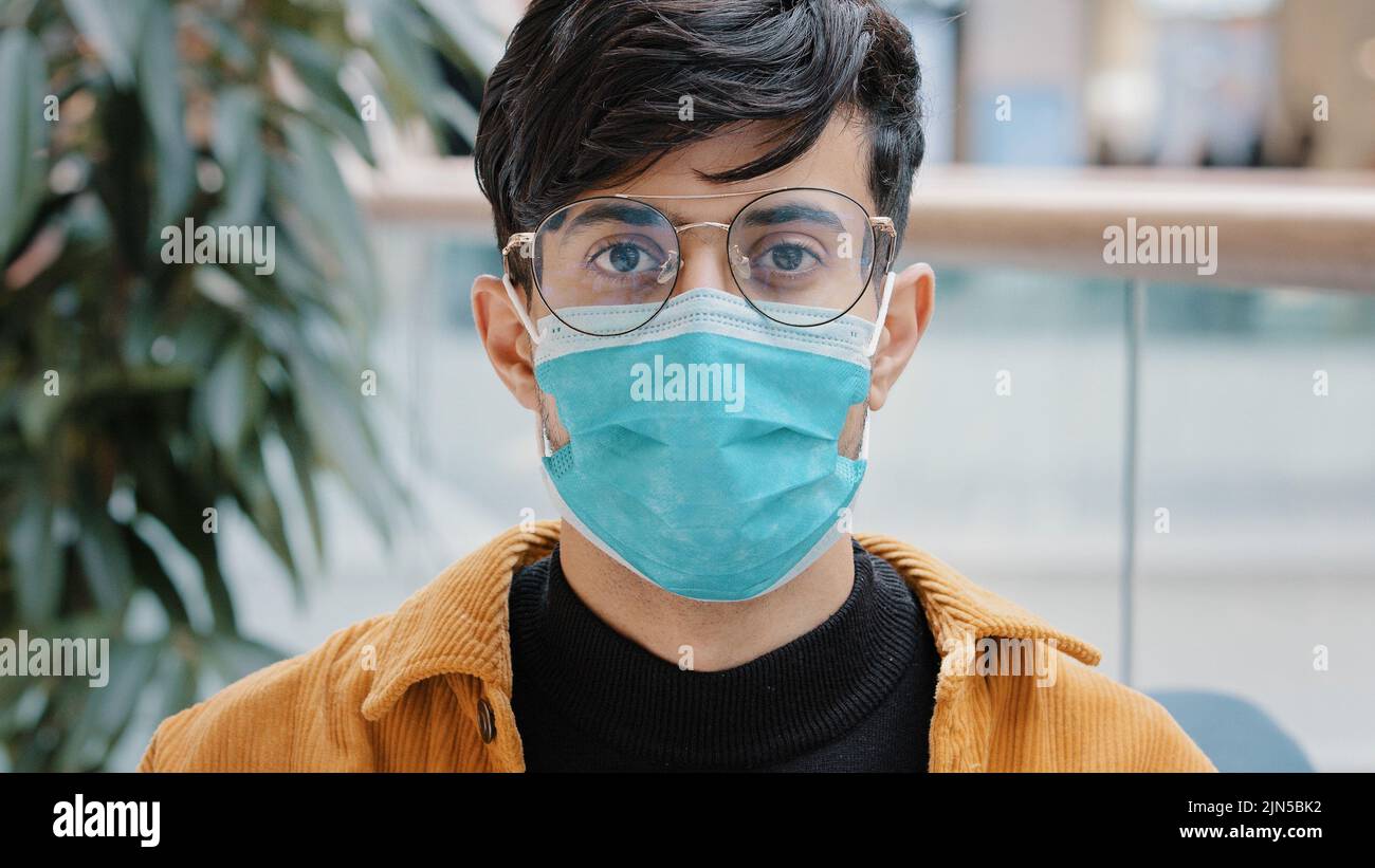 Ritratto primo piano-up giovane indiano ragazzo in maschera medica protettiva in piedi al chiuso sicuro uomo in posa guardando la macchina fotografica sicurezza personale a causa di pandemia Foto Stock
