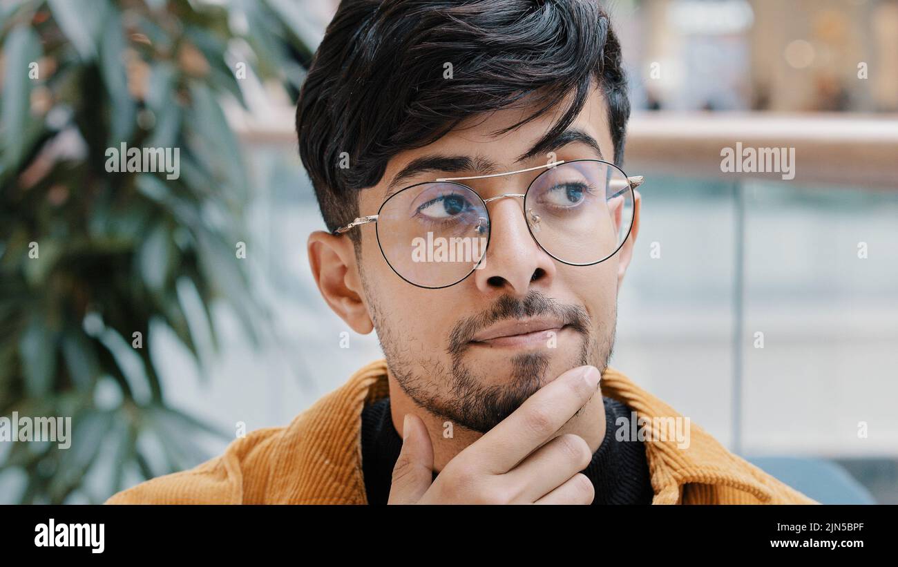 Headshot giovane e pensivo uomo indiano premuroso che tiene mano sul mento pensando in profondità nel pensiero nella ricerca decide la soluzione al problema difficile Foto Stock