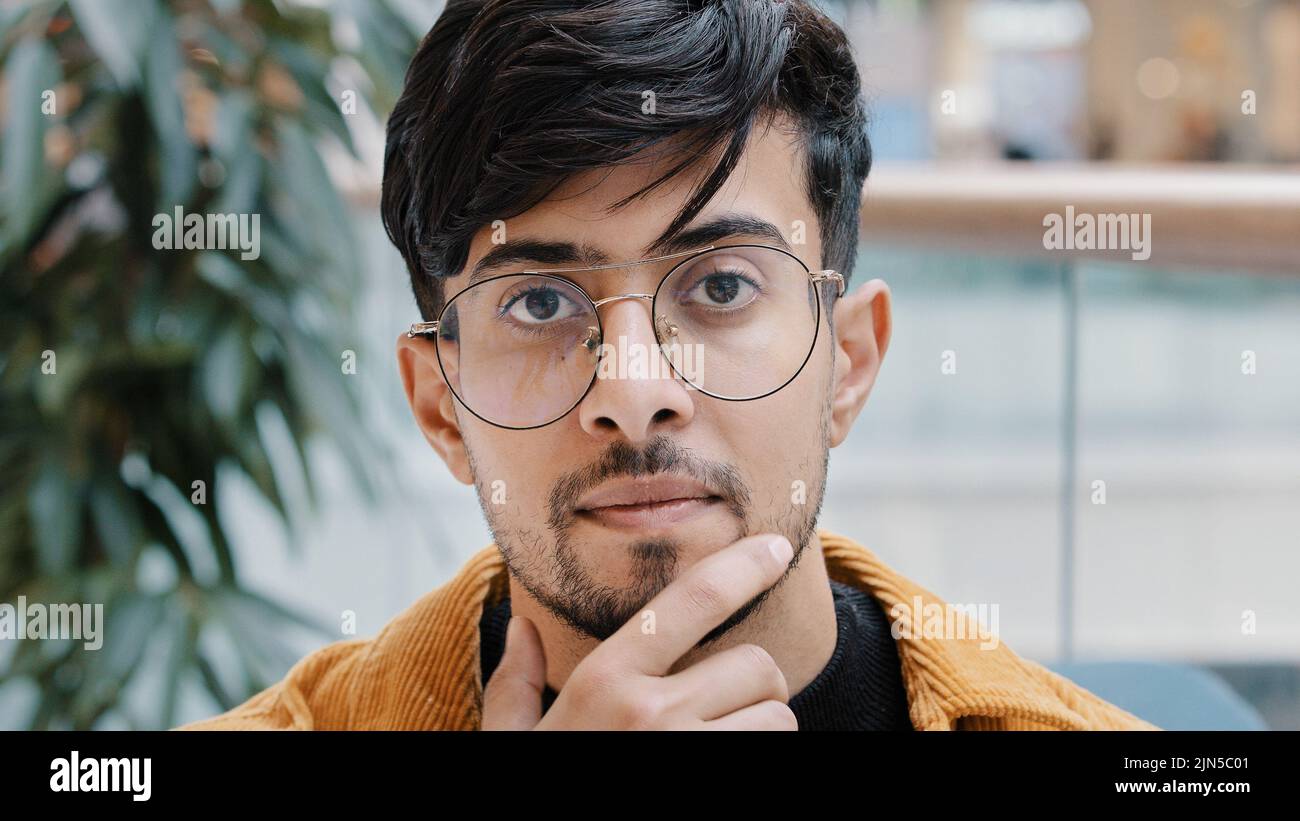 Headshot giovane e pensivo uomo indiano premuroso che tiene mano sul mento pensando in profondità nel pensiero nella ricerca decide la soluzione al problema difficile Foto Stock