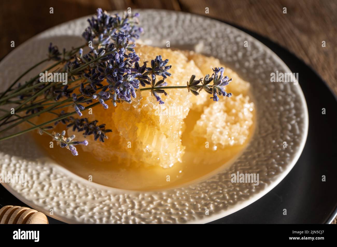 Miele e nido d'ape su un piatto bianco. Cibo dolce in una ciotola sul tavolo. Un prodotto dell'apicoltura. Fiore di lavanda. Foto Stock