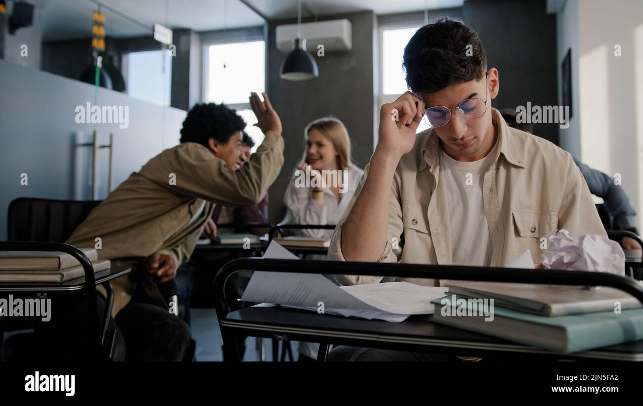 Triste preoccupato sconvolto deluso studente caucasico nerd indossare occhiali si siede in classe al banco da solo si prepara per la lezione leggere note aggressive arrabbiato Foto Stock