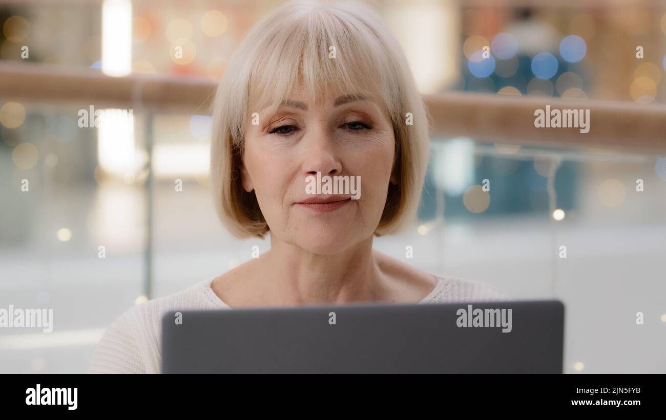 Headshot ha messo a fuoco il successo imprenditore maturo di donna d'affari che lavora sul laptop che digita l'articolo donna caucasica di mezza età che cerca le informazioni sopra Foto Stock