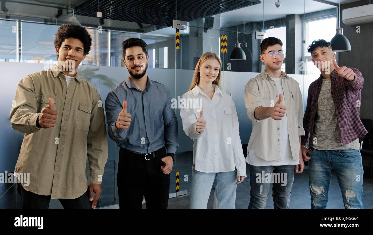 Felice gruppo professionale sicuro persone diverse dipendenti aziendali in piedi in fila guardando la fotocamera sorridente mostrando pollici in su apprezzamento migliore Foto Stock