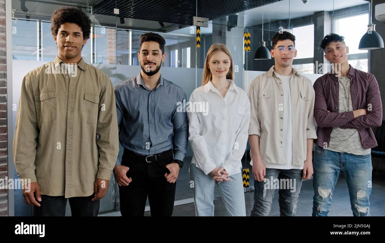 I giovani dipendenti felici si alzano in fila guardando la macchina fotografica sorridendo diversi colleghi che posano in ufficio cinque persone professionali sicure Foto Stock