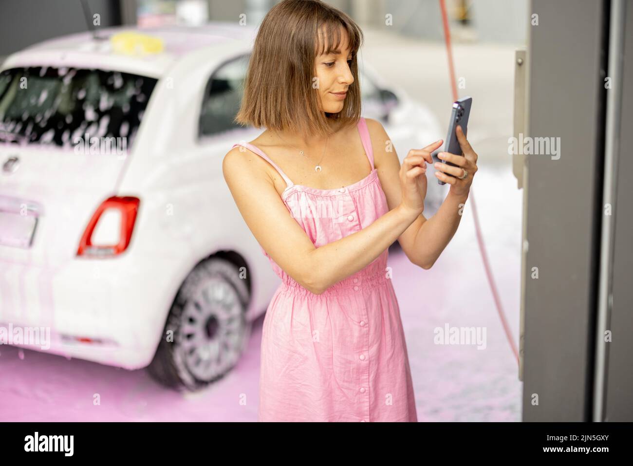 Donna che paga senza contatto con smartphone al lavaggio auto Foto Stock