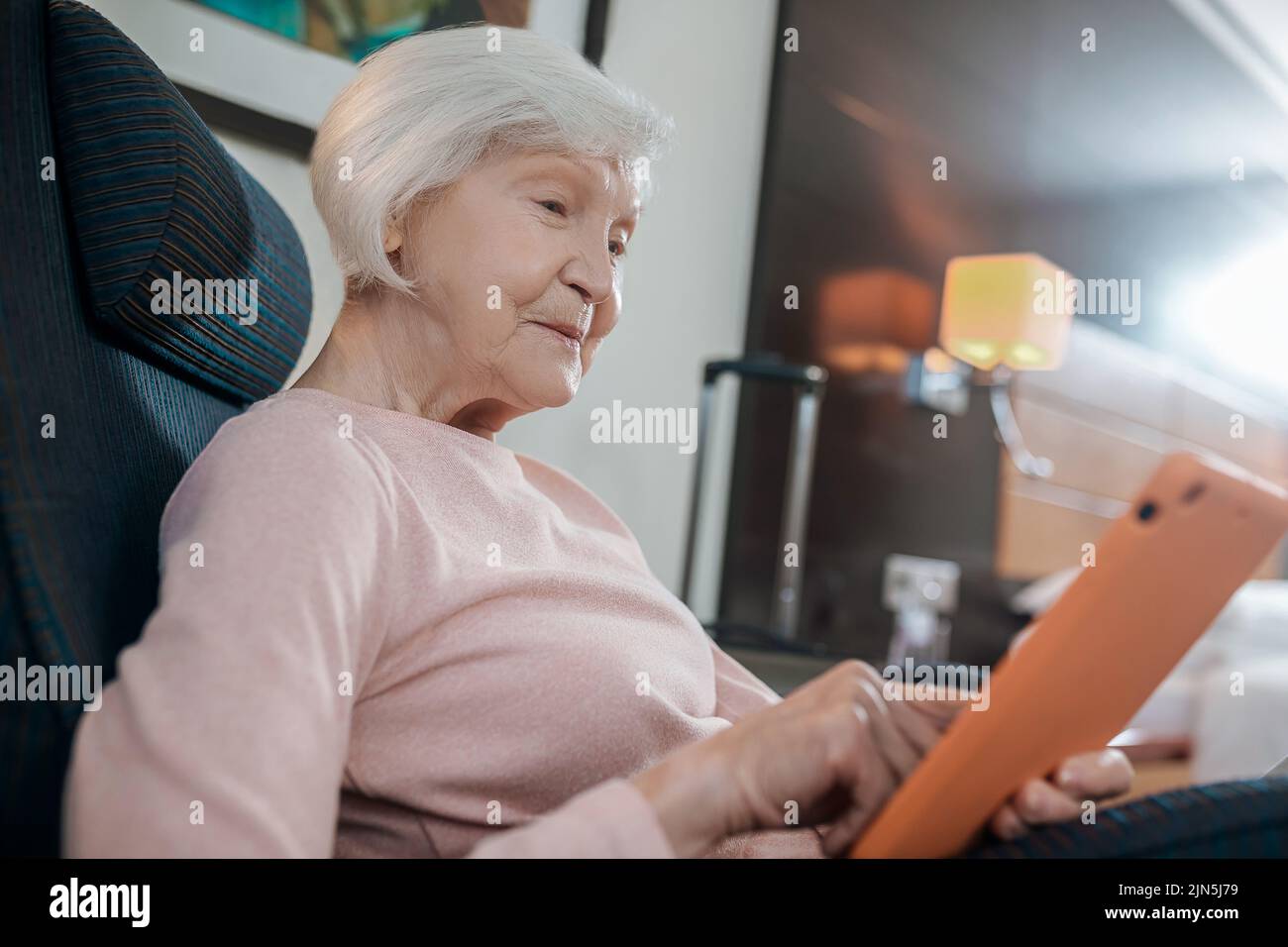Donna anziana in blusa rosa con un tablet seduto su una poltrona Foto Stock