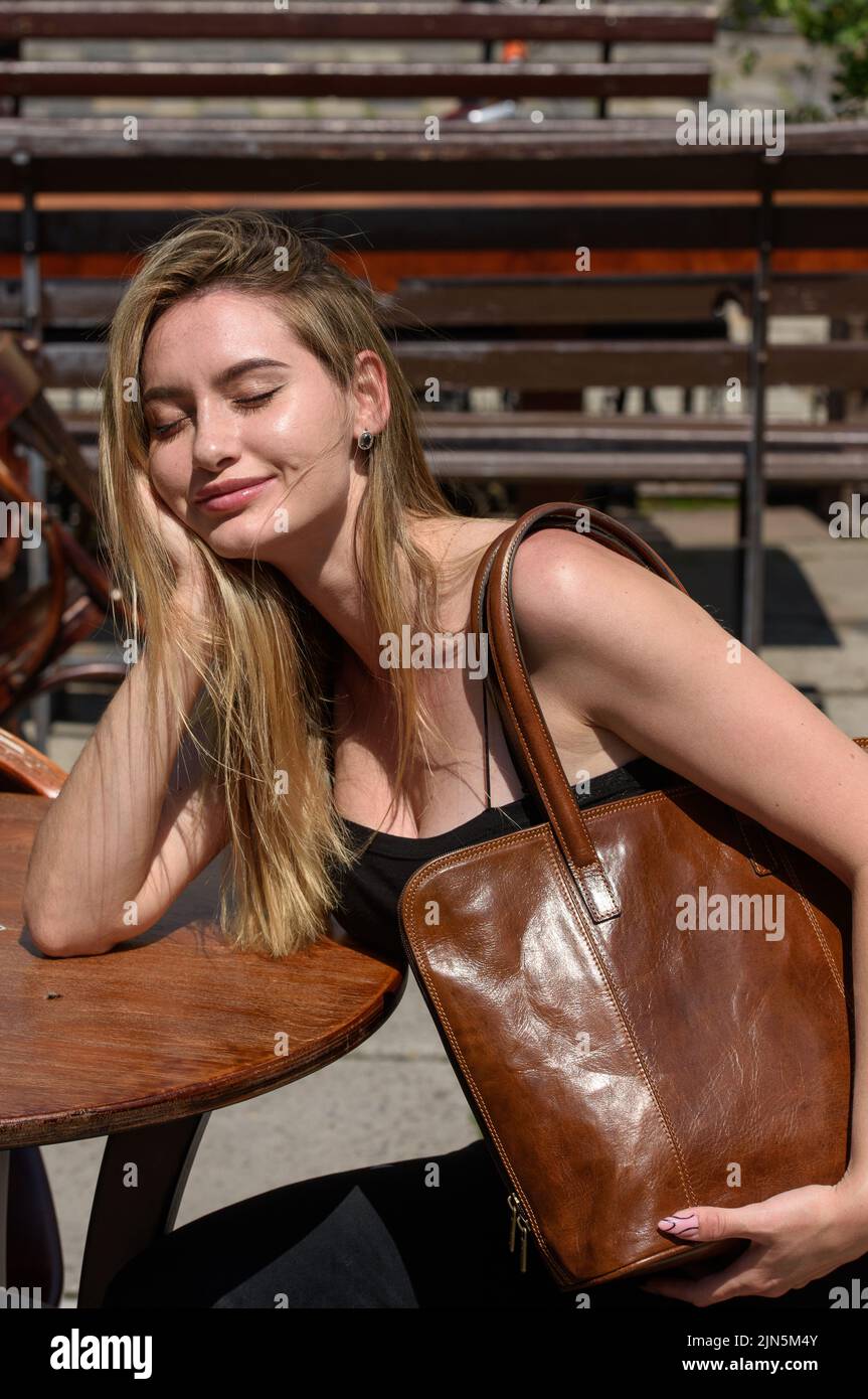 foto da vicino di una borsa in pelle marrone nelle mani di una bella donna. foto all'aperto. Ragazza in un top nero e jeans Foto Stock