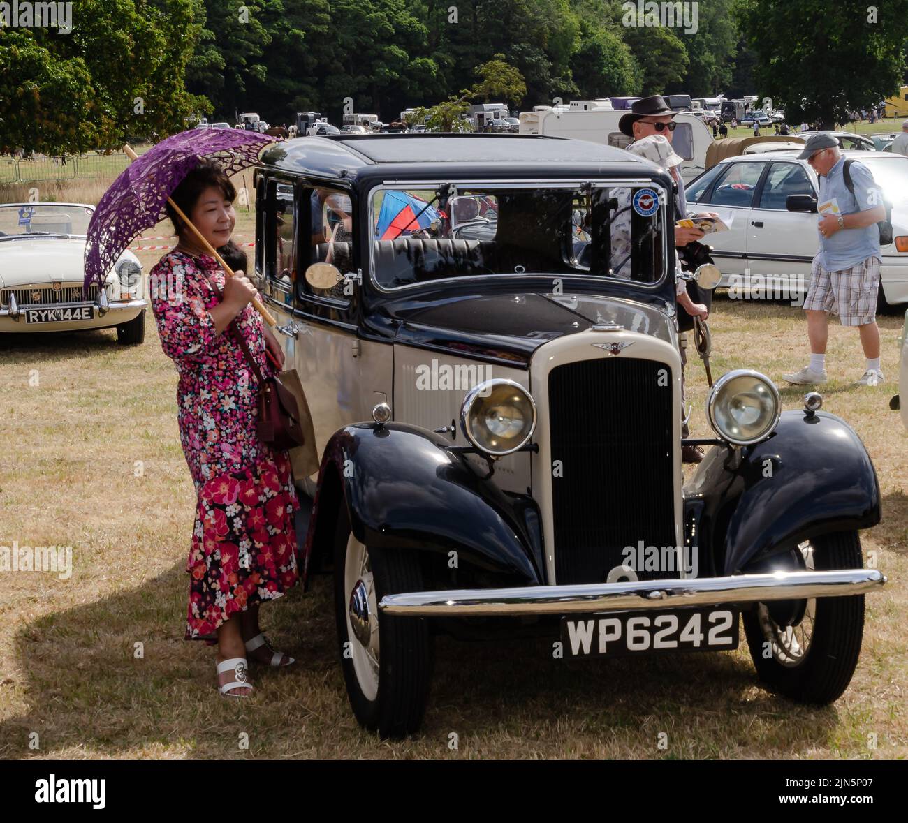Donna con ombrellone accanto alla classica auto d'epoca Foto Stock