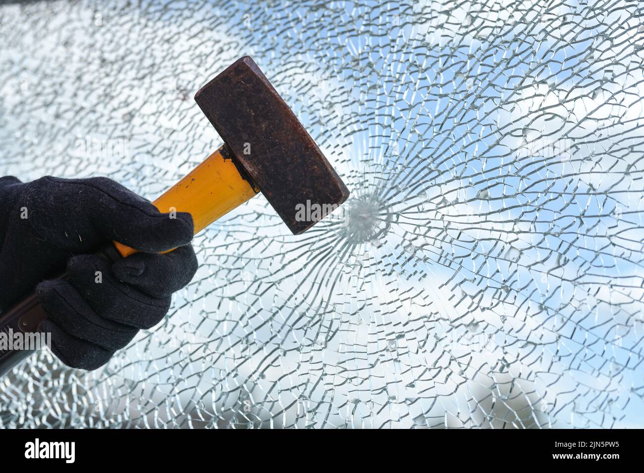 La mano dell'uomo sta colpendo una finestra dal vetro di sicurezza con un martello pesante, vandalismo e burglary concetto, copia spazio, fuoco selezionato Foto Stock