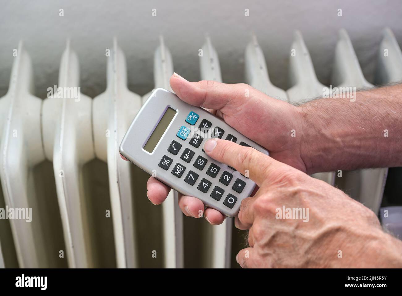 Le mani di un uomo con un calcolatore calcolano fuori i costi energetici di un sistema di riscaldamento inefficiente, concetto per la finanza domestica, inflazione, prezzi crescenti del gas Foto Stock