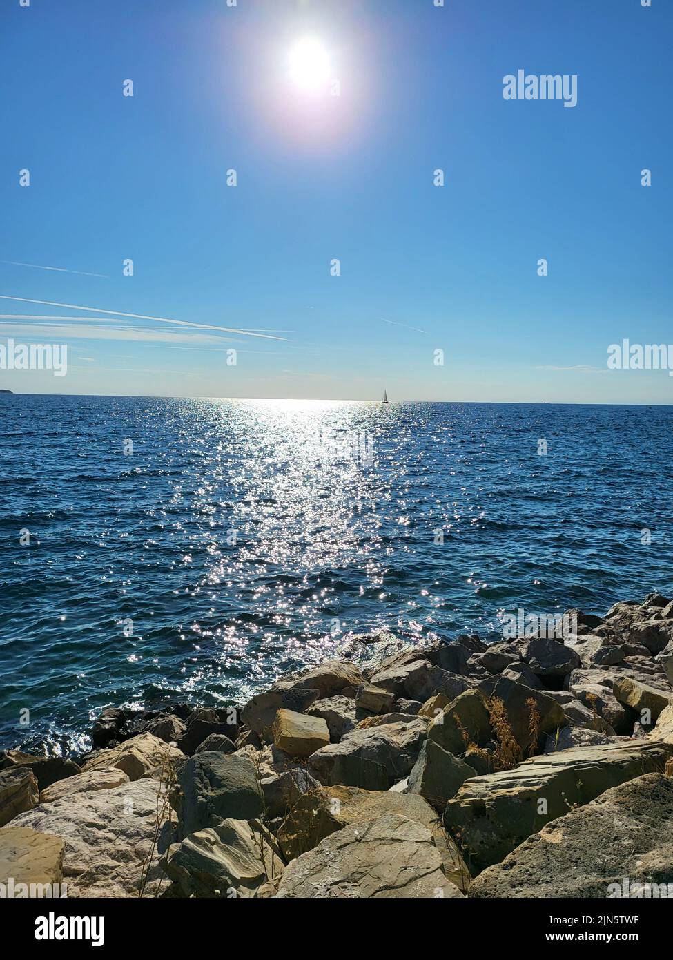 il sole è alto sul mare con costa rocciosa e riflessi leggeri sulla superficie dell'acqua Foto Stock