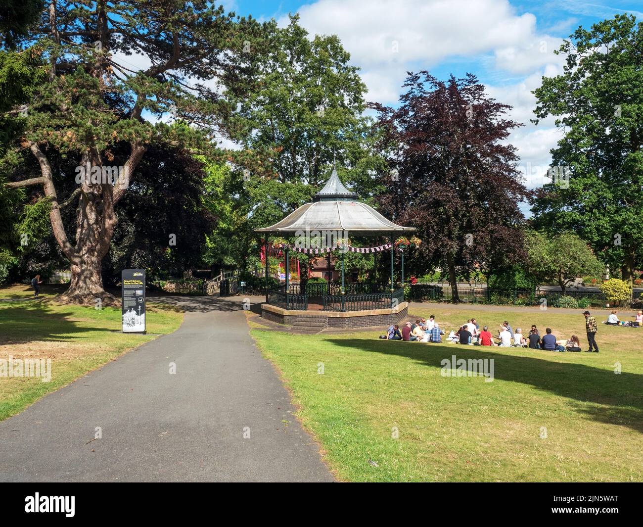 Persone che siedono sull'erba presso il Bandstand in Priory Park Great Malvern Worcestershire Inghilterra Foto Stock