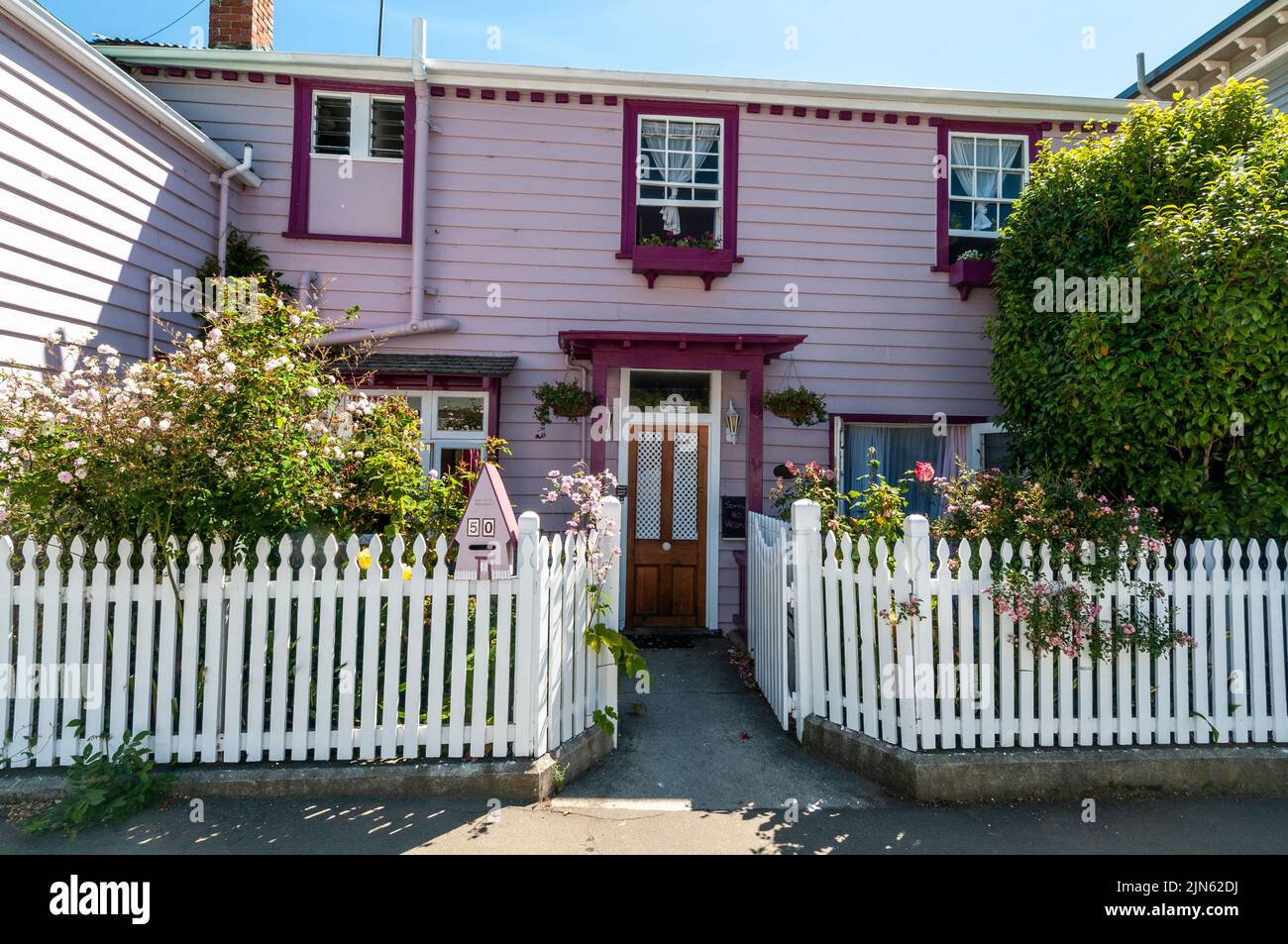 Una delle molte case in legno-costruito pioniere residenziale con un giardino di rose recintato nella piccola città di Akaroa sulla penisola di Banks sull'Isola Sud di Foto Stock
