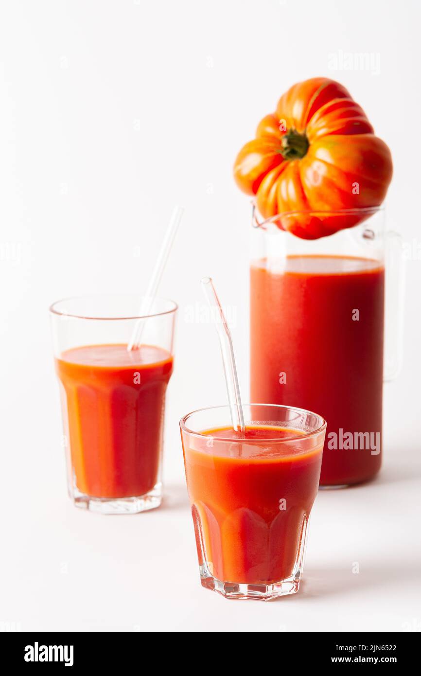 Succo di pomodoro appena spremuto in bicchieri e una caraffa con pomodori su sfondo bianco Foto Stock