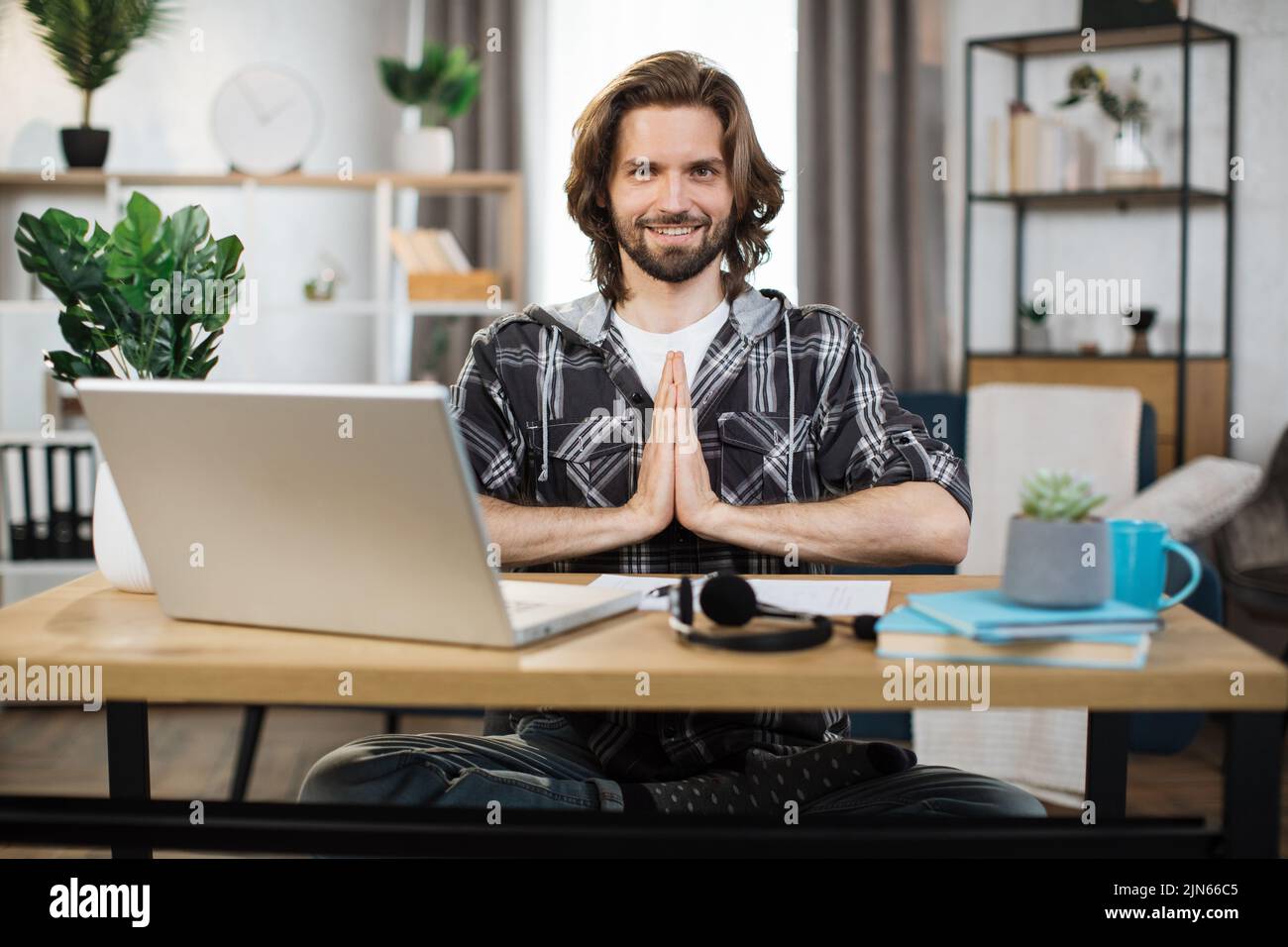 Giovane uomo barbuto freelancer seduto a tavola con gli occhi aperti e alleviare lo stress da meditazione sul posto di lavoro. Concetto di relax e armonia, nessun sollievo senza stress sul lavoro. Foto Stock
