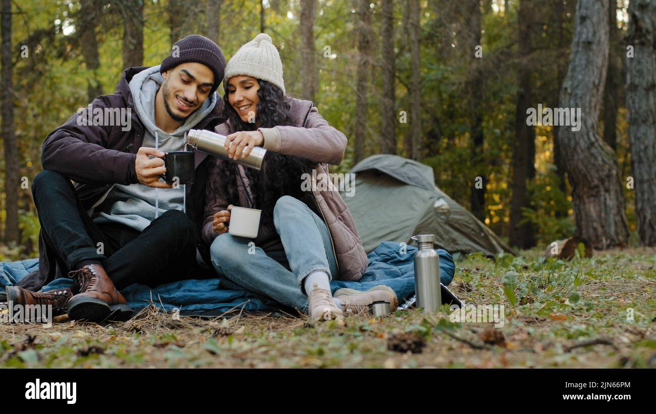 Giovane coppia in amore viaggiatori si siede in natura riposo bere tè da thermos godere di bevanda calda riposo parlare sorridendo sentire piacere viaggio Foto Stock