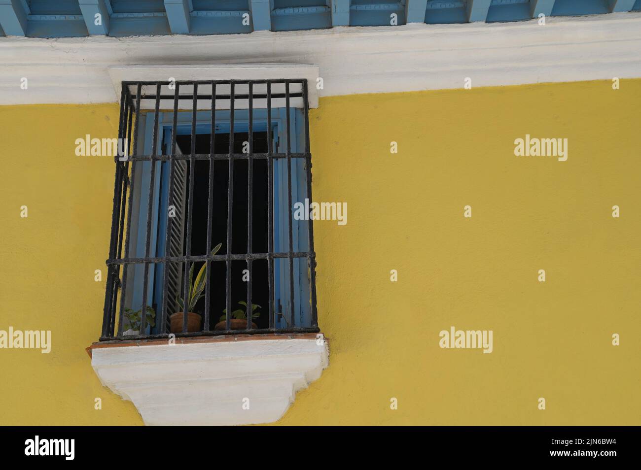 Vecchio edificio coloniale spagnolo finestra in legno con griglie in ferro battuto artigianale su un muro di stucco giallo a Old Havana, Cuba. Foto Stock