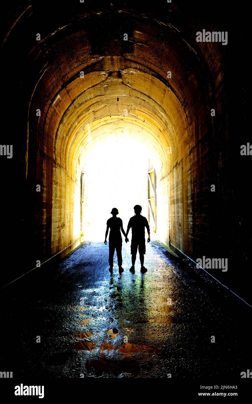 Due persone innamorate che tengono le mani in silhouette silhouette silhouette al tunnel uscire insieme Foto Stock