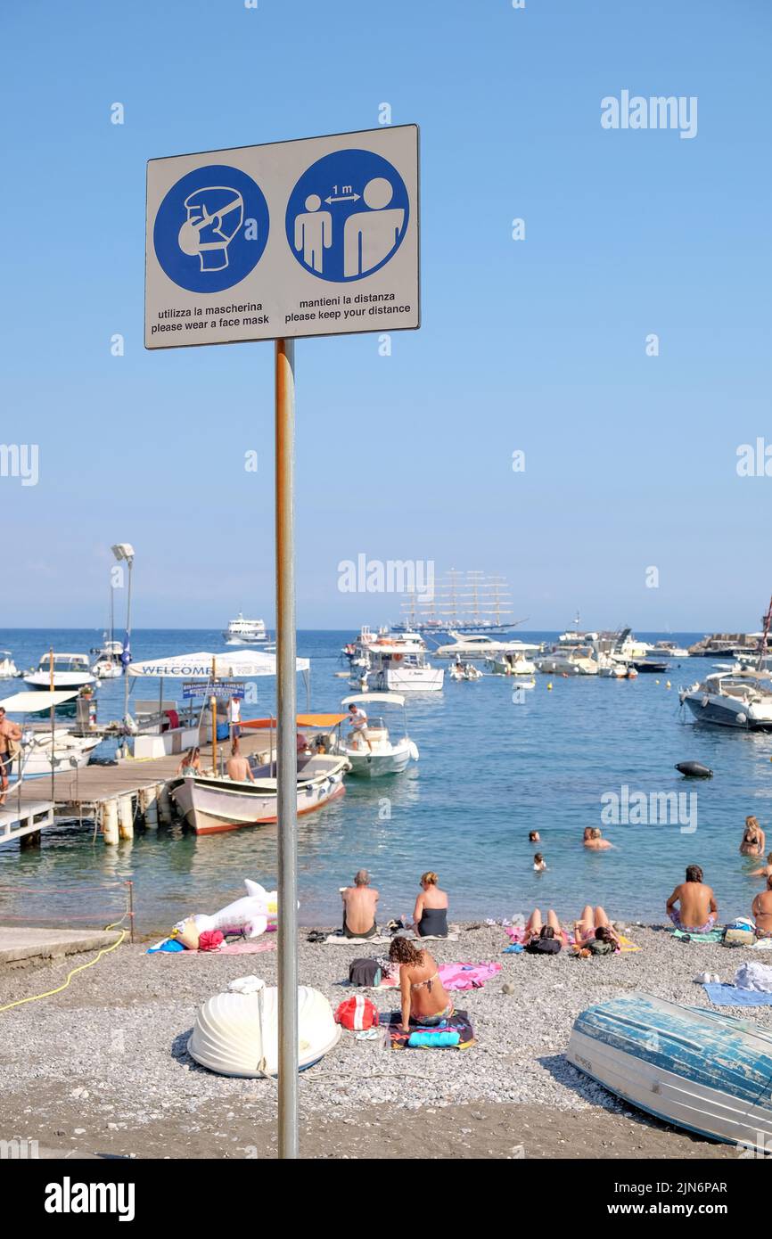 Informazioni sul Covid cartelli segnaletici sul lungomare del villaggio di Positano in Italia con spiaggia e lungomare sullo sfondo.Social distanze e maschere. Foto Stock